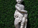 a statue of a boy holding a bird in a garden