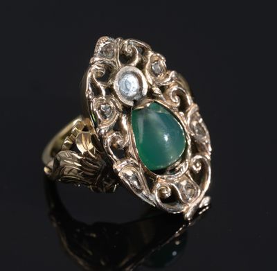 gros plan d'une bague en or avec une pierre verte et des diamants