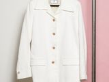 La veste blanche est suspendue à un cintre devant un mur rose et blanc.
