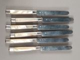 four knives are lined up on a table with a knife in front of them