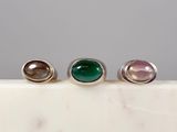 three silver rings with green and pink stones on a marble surface