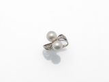 une bague en perle blanche et diamants posée sur une surface blanche