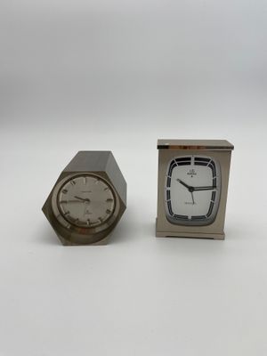 une petite horloge en argent et une autre petite horloge en argent posées sur une surface blanche