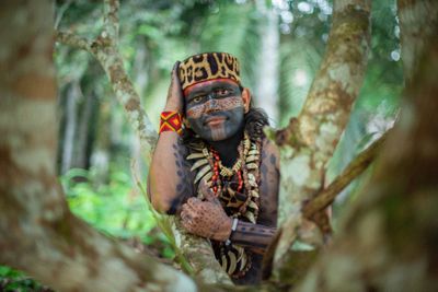 un homme assis dans un arbre, le visage barbouillé de peinture