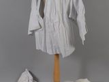 un mannequin vêtu d'une chemise blanche et entouré d'une pile de vêtements