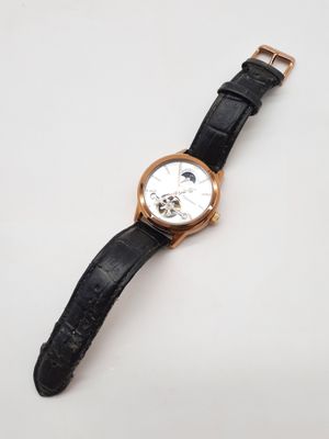 gros plan d'une montre sur une surface blanche avec un bracelet noir