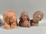 three clay heads of people sitting next to each other on a white surface