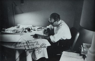 photographie en noir et blanc d'un homme assis à une table, en train d'écrire sur une feuille de papier