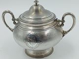 une théière en argent avec son couvercle, posée sur une table blanche