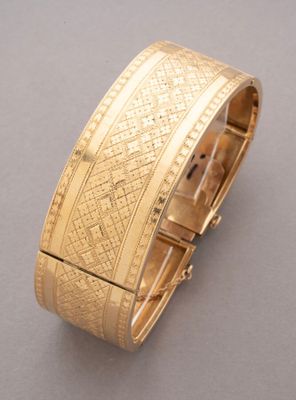 gros plan d'un bracelet en or sur une surface grise