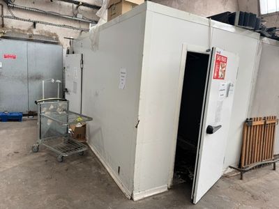 un grand réfrigérateur blanc dans une pièce où se trouve un chariot métallique