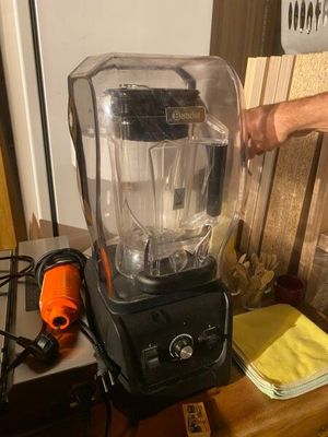 a blender sitting on a table with a person ' s hand on it