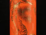 un vase orange orné d'un motif doré, posé sur une surface noire