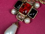 necklace with a red, black, and white pendant and pearls on a pink background