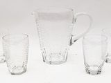sept verres et un pichet posés sur une surface blanche