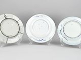three white and blue china plates on stands against a gray background