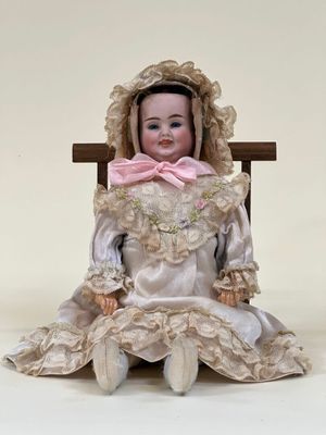 une poupée assise sur une chaise, avec un nœud rose