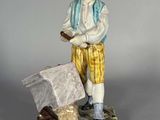 figurine représentant un homme coiffé d'un chapeau et vêtu d'un pantalon jaune, tenant un sac