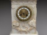 une petite horloge blanche avec un cadran doré, posée sur un socle