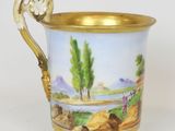 a gold cup with a painting of a landscape on it