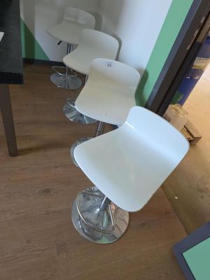 Plusieurs chaises blanches sont alignées en rang devant un mur vert.
