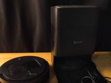 two black speakers sitting on top of a wooden table next to a black bag