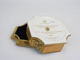 an antique gold and white box with a black lid on a white surface