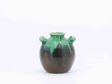 a green and black vase sitting on a white surface