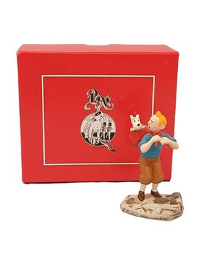 La figurine se trouve dans une boîte rouge sur laquelle est représenté un garçon tenant un chien dans ses bras.