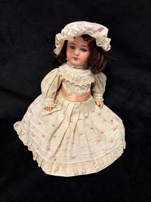 une poupée ancienne vêtue d'une robe blanche et d'un bonnet, sur fond noir