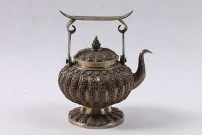 une théière ancienne en argent, munie d'une anse et posée sur un socle