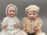 deux poupées en porcelaine représentant des bébés assis l'un à côté de l'autre sur une surface grise