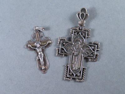 deux pendentifs en forme de croix en argent, avec un crucifix, posés sur une table