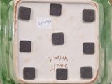 someone is holding a green and white square shaped plate with black squares on it