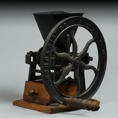 un moulin à café à l'ancienne posé sur un socle en bois, sur fond gris