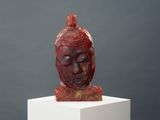 sculpture représentant une tête de femme posée sur un socle blanc, sur fond gris