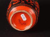 a red vase with black designs on it on a black surface