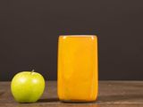 an apple next to a glass of juice on a wooden table