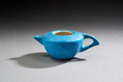 théière en céramique bleue avec une anse, posée sur un fond gris