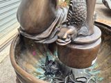 a bronze statue of a woman holding a fish in a bowl
