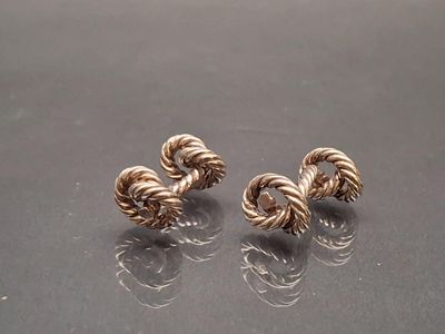 paire de boucles d'oreilles en forme de corde torsadée de couleur dorée sur un fond noir