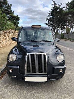un taxi noir garé sur le bord de la route, devant un mur de pierre