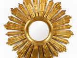une photo d'un miroir doré en forme de soleil rayonnant accroché à un mur blanc
