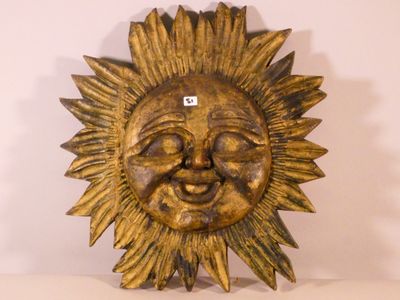 a gold sun face hanging on a white wall