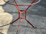 une table en métal rouge avec un plateau en verre, posée sur le trottoir