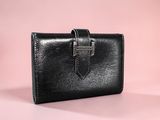 a black leather wallet with a metal clasp on a pink background