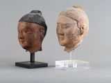 paire de sculptures représentant des têtes asiatiques posées sur un socle en acrylique, sur fond gris