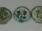 trois pièces de monnaie romaines anciennes, dont l'une représente une tête de lion et l'autre est une