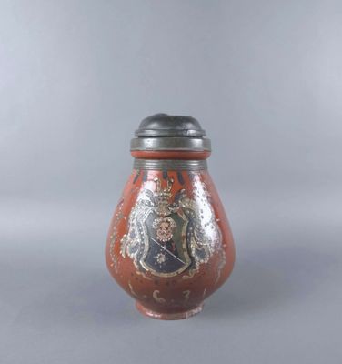 un vase rouge avec un couvercle noir posé sur une table