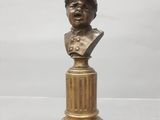 un buste en bronze représentant un homme coiffé d'un chapeau, posé sur un socle
